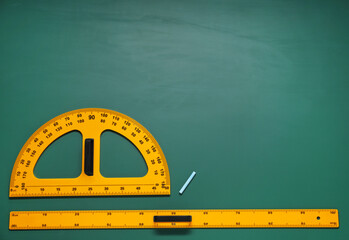 Protractor, ruler and chalk on green chalkboard, flat lay. Space for text