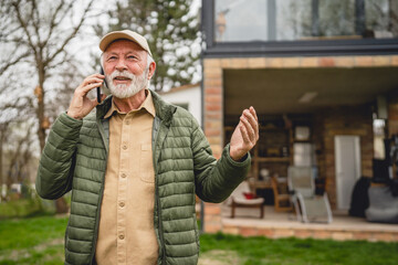 One senior man stand in front of tiny house in day use smart phone