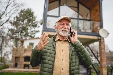 One senior man stand in front of tiny house in day use smart phone