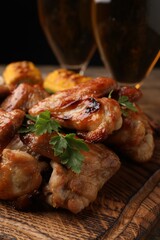 Delicious baked chicken wings and glasses with beer on wooden table, closeup