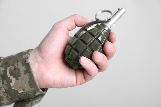 Soldier holding hand grenade on light grey background, closeup. Military service