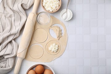 Process of making dumplings (varenyky) with cottage cheese. Raw dough and ingredients on white tiled table, flat lay. Space for text