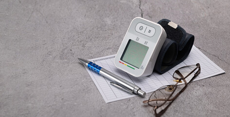 Automatic digital wrist blood pressure monitor, pressure monitoring chart, pen, glasses on gray background - obrazy, fototapety, plakaty