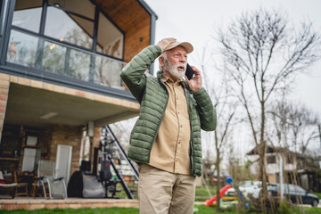 angry senior man stand in front of tiny house in day use smart phone