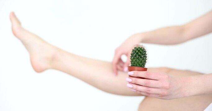 Woman holding cactus in hand against background of smooth delicate skin of legs closeup 4k movie slow motion. Laser epilation skincare concept