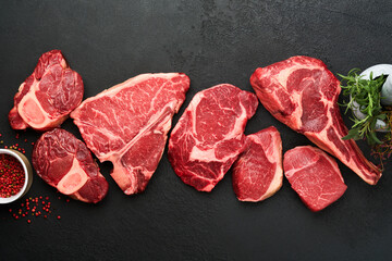 Raw prime steaks. Variety of fresh black angus prime meat steaks T-bone, New York, Ribeye, Striploin, Tomahawk cutting board on black or dark background. Set of various classic steaks. Top view.