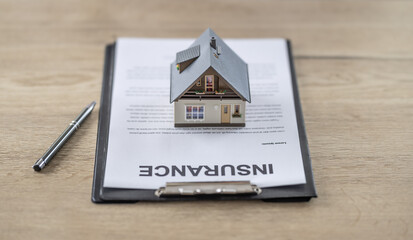 Obraz na płótnie Canvas House insurance contract concept with a house model on top of the paperwork lying on a table next to a pen
