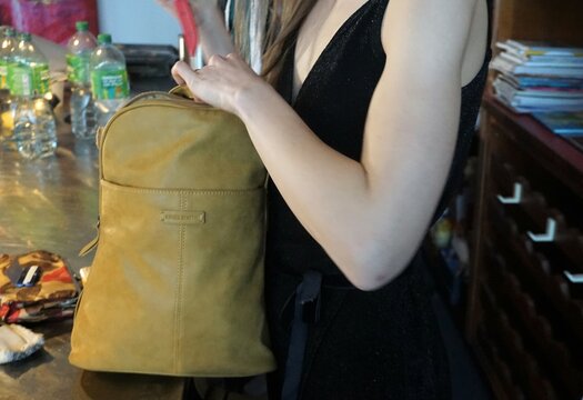 Junge schlanke Frau mit schwarzem Tr&auml;gerkleid mit braunem Lederrucksack hinter Theke in Restaurant 