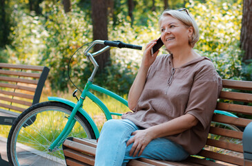 Portrait happy older woman sitting on park bench talking with cellphone