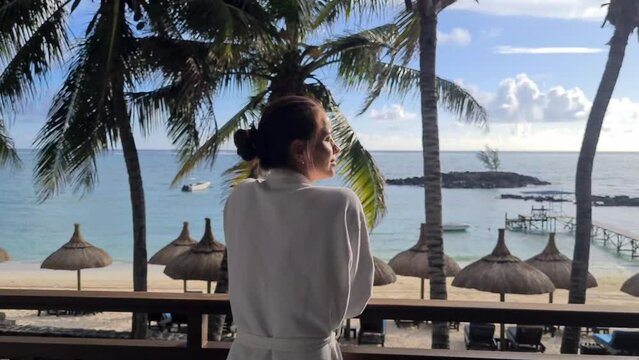 Beautiful woman stands and enjoys sea or ocean view on balcony on paradise island. Tourism vacation and travel