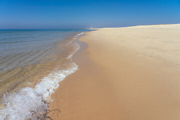 Idyllic beach of the Culatra island in the Algarve region of Portugal with the famous lighthouse of Farol in the background in a sunny day.