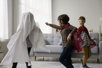 Three active naughty boys wearing super hero costumes, playing fighting role games at home,...