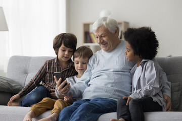 Happy elderly grandfather and diverse grandchildren boys speaking on family video call, using...