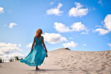 Beautiful blonde woman on hot sand with blue sky in the background. Photo taken on the shifting dunes over the Baltic Sea in Łeba, Poland. Photo with a shallow depth of field with blurred background. - obrazy, fototapety, plakaty
