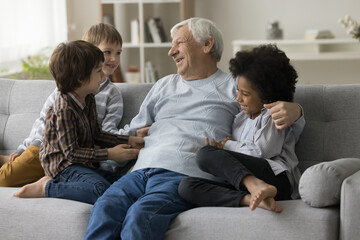 Cheerful little multiethnic grandsons tickling positive senior grandfather. Happy grandpa hugging,...