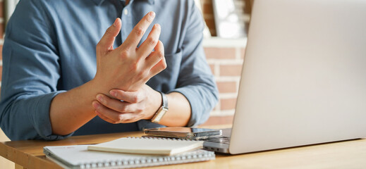 close up employee man massage on his hand and arm for relief pain from hard working on the desktop table at hoe office for stiff or cramp symptom or carpal tunnel syndrome concept