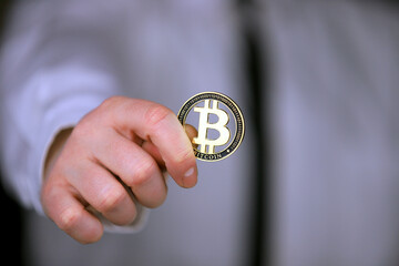 A businessman in a white shirt and black tie holds a physical version of bitcoin in his hands.