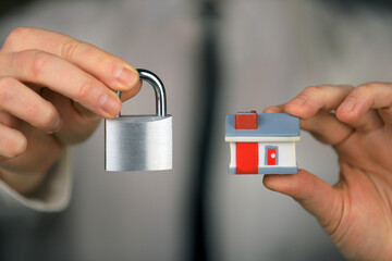 A businessman in a white shirt and black tie holds a silver padlock and miniature house in his hands. Home security.