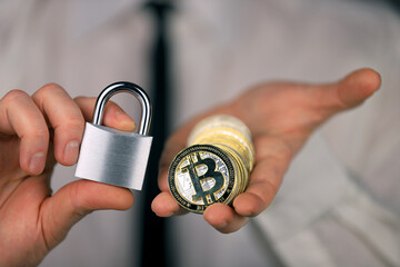 A businessman holds a silver padlock and physical version of bitcoin in his hands. Prohibition of cryptocurrencies, regulations, restrictions or security, protection, privacy.