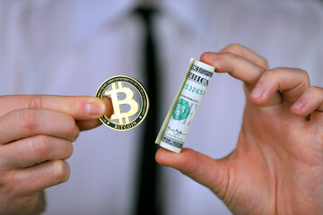 Businessman holding bitcoin and bundle of dollars in his hands.