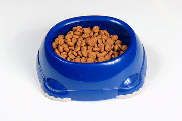 Top view of brown kibble pieces for cat feed in a blue plastic bowl on white background, cat food, dog food