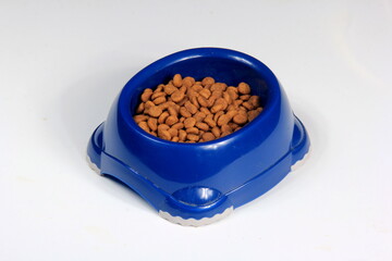Top view of brown kibble pieces for cat feed in a blue plastic bowl on white background, cat food,...