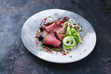 Traditional Commonwealth Sunday roast as sliced cold cuts roast beef with zucchini and capers in...