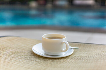 A cup of coffee on the sunbed over a swimming pool, vacations concept