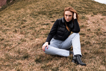 Naklejka na ściany i meble Young woman in black jacket and blue jeans sit dry grass in Norway