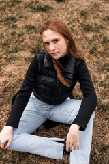 Young woman in black jacket and blue jeans sit dry grass in Norway