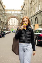 Young woman in black jacket and jeans with coffee on the street urban fashion