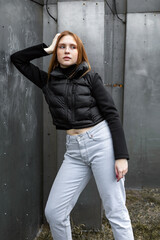 Fototapeta na wymiar Young woman in black jacket and jeans posing near steel wall. Fashion cold tone