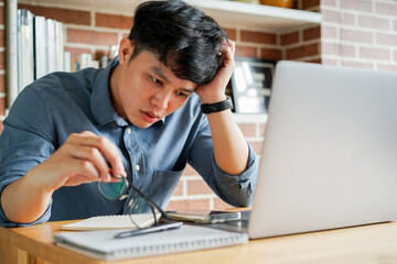 close up young asian employee man feeling headache about migraine after working hard in home office...