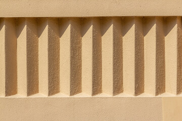 Beige exterior stucco wall with repeating details. Rough surface in the sun with shadows. Rough...