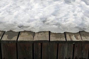 Melting on spring snow on the old brown wooden boards surface outdoors front view close up