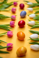 Weiße und pinkfarbene Tulpen liegen in zwei Reihen, in der Mitte liegen gefärbte Hühnereier. Der Schärfepunkt liegt auf einem Ei.