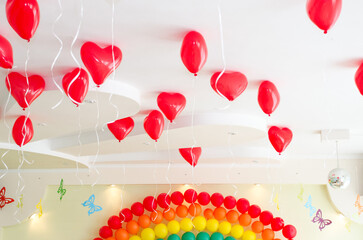 Red heart shaped inflatable helium balloons hang from the ceiling during a birthday party
