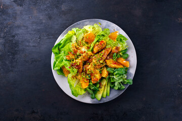 Traditioneller deutscher Eisberg und Feldsalat serviert mit Hähnchen, Avocado und Orangenscheiben mit pikanter süß saurer Currysauce serviert als Draufsicht auf einem Designteller mit Textfeld 