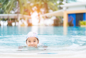 Asian child holiday relax or kid girl wearing swimsuit and cap on swimming pool and smile with...