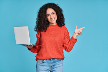 Young happy latin woman holding laptop pointing aside isolated on blue background. Smiling female...
