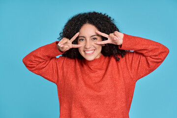 Fototapeta na wymiar Young happy positive pretty latin woman having fun isolated on blue background. Smiling funny curly cool girl female model showing victory hands sign gesture standing at color wall. Portrait.