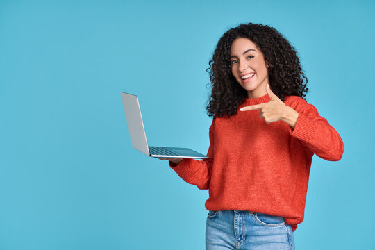 Young Happy Latin Woman Pointing At Laptop Isolated On Blue Background. Smiling Female Model Holding Computer Presenting Advertising Job Search Or Ecommerce Shopping Website.