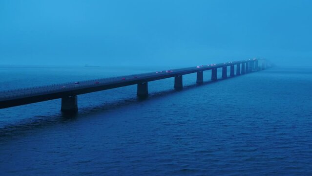 Aerial of traffic over the bridge Storebæltsbroen in Denmark. There is a heavy fog, and it is during the blue hour. 4K