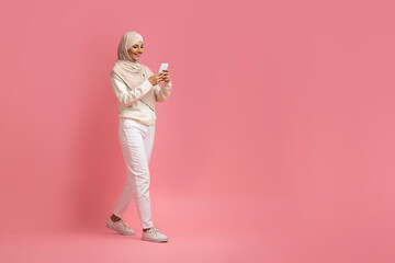 Mobile Communication. Muslim Woman In Hijab Walking With Smartphone On Pink Background