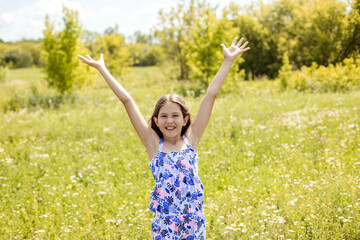 Naklejka na ściany i meble Portrait of a joyful pretty teenage girl with her hands raised in a beautiful summer field