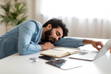 Fototapeta premium Tired indian male freelancer sleeping at desk in home office