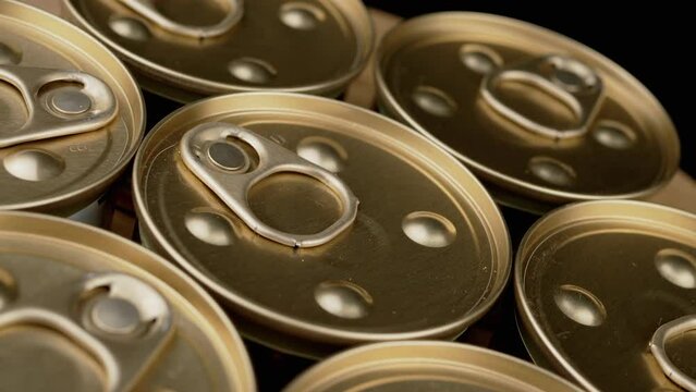 Close up, Rotation of Metal Cans with Canned Food or Pate on Black Background. Angle top view. Golden cans with pull rings. Canned tourist food or wet pet food. Military, humanitarian aid to soldiers.