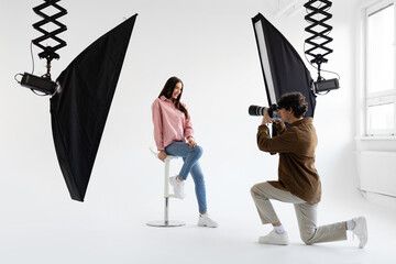 Professional photographer taking picture of young woman, having photoshoot in studio with lighting...