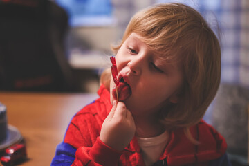 Cute little child in spider man costume eating a red lollipop in form of the number five during his birthday party. Small boy enjoys licking a tasty sugar lollipop. © Татьяна