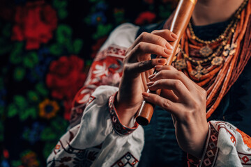 Hands of woman playing on woodwind wooden flute - ukrainian sopilka on colorful